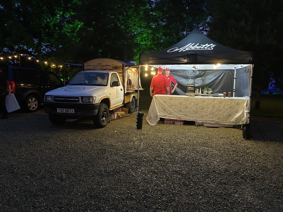 The pizza truck and branded gazebo lit up at a corporate evening event, crew in red uniform
