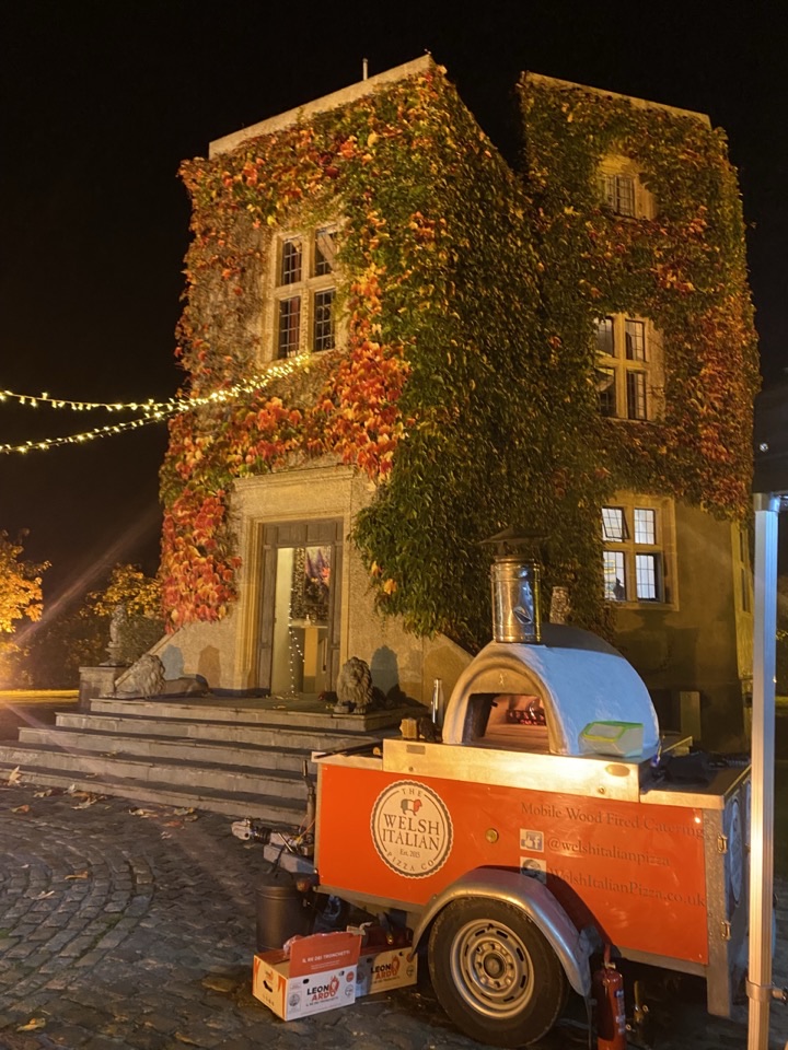 The branded oven trailer parked outside an ivy-covered house at an evening party
